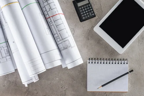 Rolled architectural blueprints, a tablet, and a notepad on a studio desk