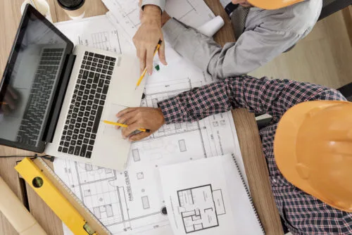 Two construction managers reviewing blueprints with a laptop on the job
