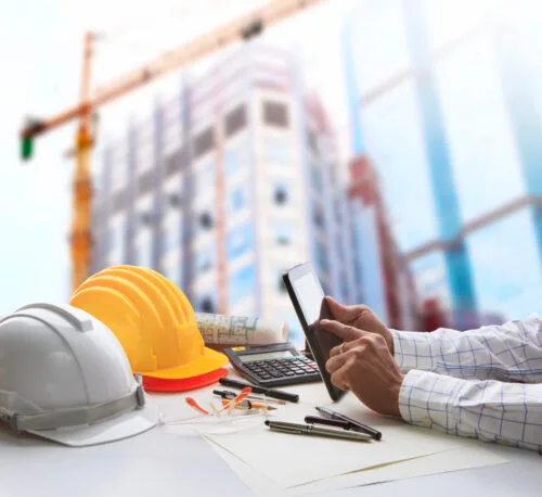 A hard-hat construction worker using a tablet on site with a crane and building behind, managed IT support for construction
