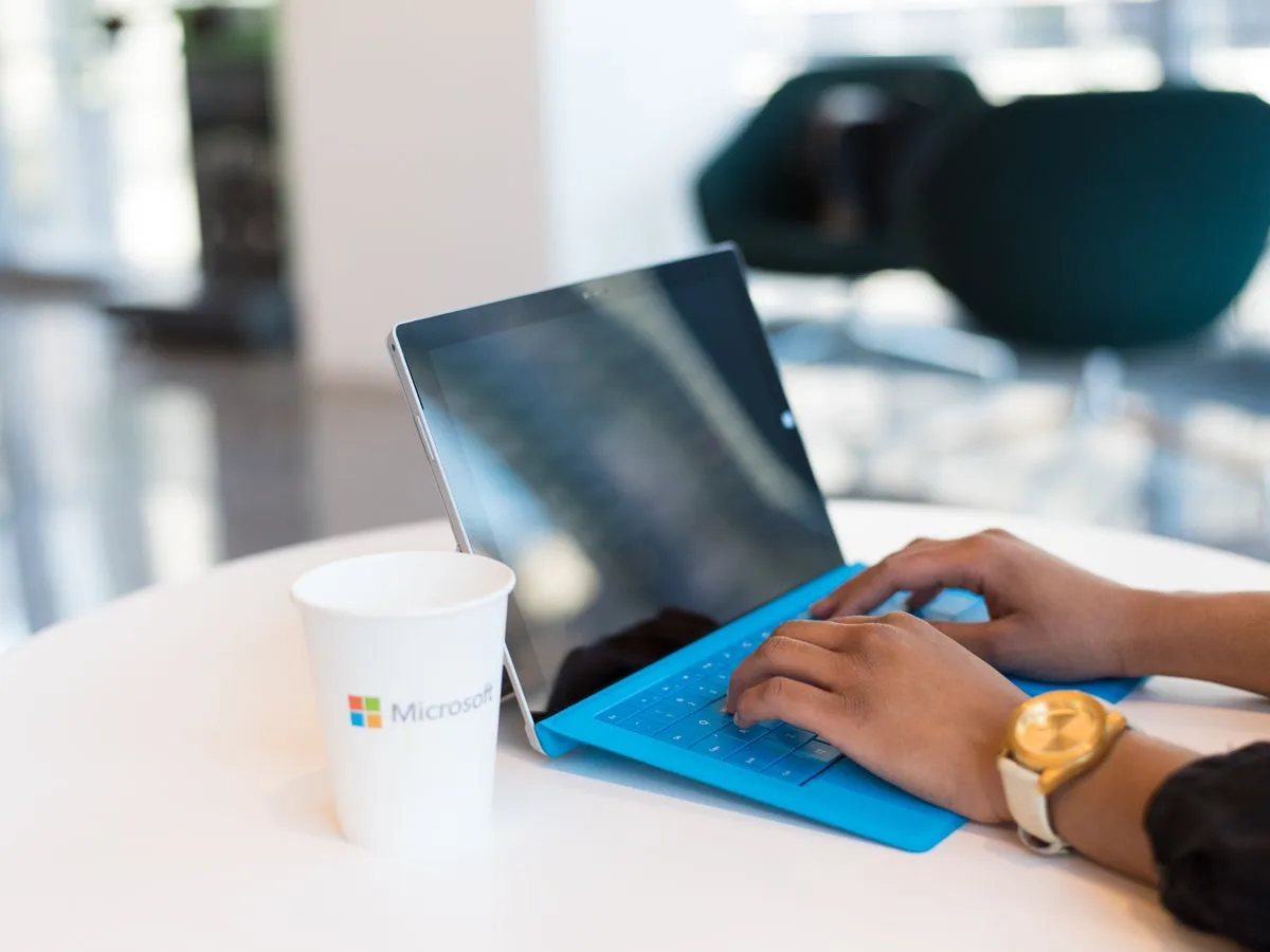 A person working on a Microsoft Surface device beside a branded Microsoft cup, representing Microsoft 365 productivity software